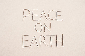 Peace On Earth holiday message handwritten on smooth sand beach