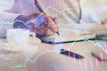 Double exposure of man's hands writing notes of stock market with forex chart.