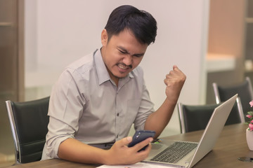 Asian businessmen are happy to work successfully with laptop and paper on the wooden table in the office building.