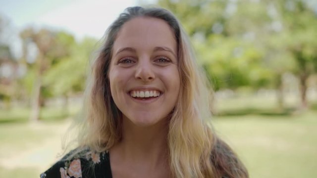 Portrait of a blonde young woman looking to camera feeling joyful and happy at outdoors - smiling into the camera