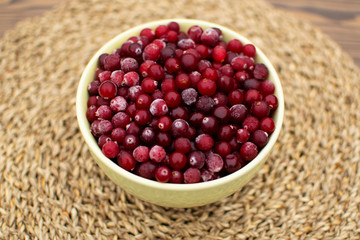 Big green bowl full of frozen berries, cranberries, standing at the table in the morning during breakfast at wicker napkin in the village