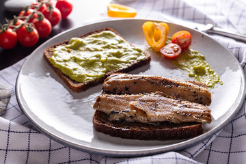 Homemade smoked herring and avocado open sandwiches with rye bread on light grey plate, top view 