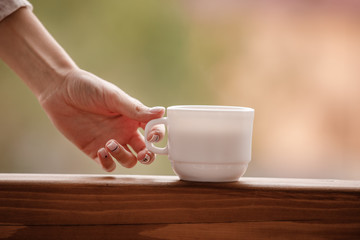 Morning coffee cup. Female hand holds white cup of morning hot drink - coffee or tea on the balcony on the background of mountain nature.