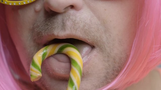 Caramel candy licks stylish man with pink hair close up.