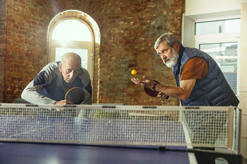 Senior men playing table tennis in workplace, having fun. Friends in casual clothes play ping pong...