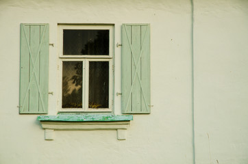 The wall of the farmhouse is neatly covered with light stucco. There is a window with open light green shutters and a metallic tint. Background. Texture.