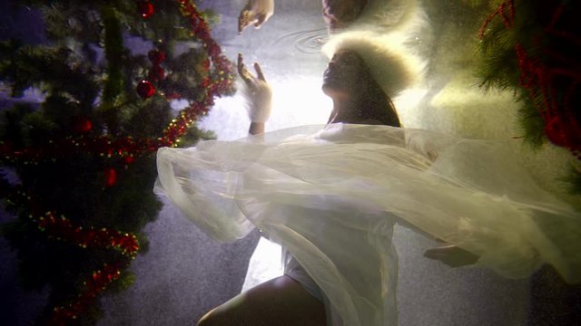 woman looks like Snow queen is floating under water in pool in Christmas decorations