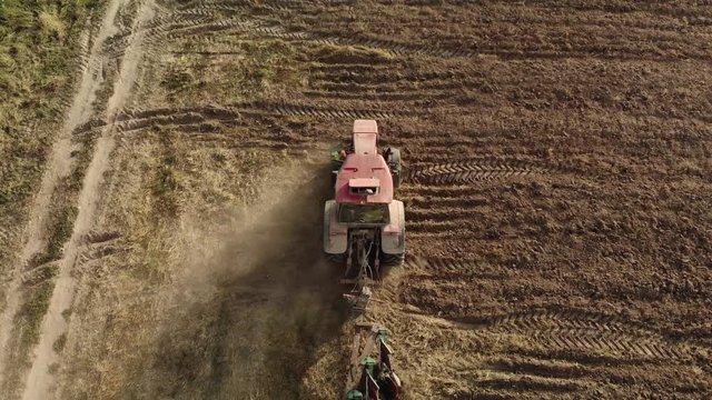 Aerial shot of a powerful tractor with a plow cultivating the field and raising huge clouds of brown suffocating dust on the agricultural field. The concept of a dry lean year, soil erosion