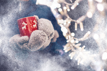 Christmas light and a woman holding in hand a red mug with hot drink