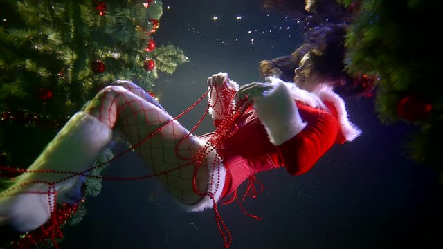 underwater Christmas fairy tale, woman in erotic suit of Santa Claus is floating in pool