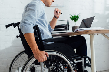 Cropped view of man sitting in wheelchair by notebook at workplace