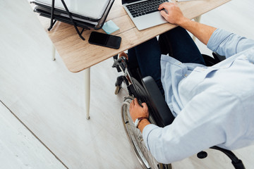 Cropped view of man in wheelchair using laptop at workplace