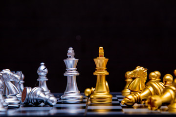 Selective focus gold King chess with followers board game in competition concept, face to face leadership, strategy, business and teamwork symbol by chess board game with dark black background