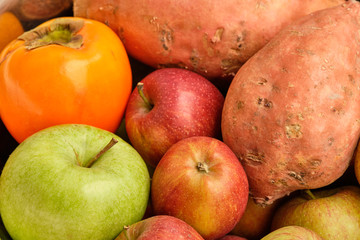 Colorful background with healthy fruits and vegetables like apples, kaki and sweet potatoes lying close together.
