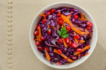 Red cabbage salad with carrots and pomegranate in a white bowl on a linen background. Detox and...
