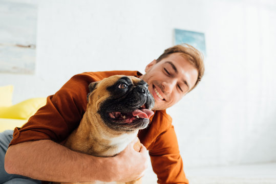 Happy man hugging french bulldog in living room