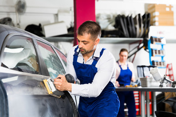 Mechanic grinding car body after puttying