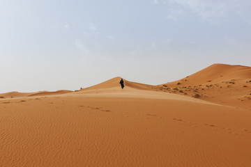 Beautiful desert dunes landscape in orange color, and man walking on the sand at sunset.