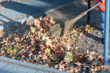 A cleaning lady cleans the dead side of the maple leaves from the sidewalk.