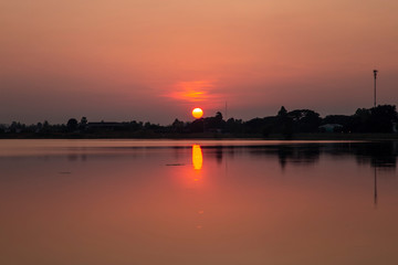 Fototapeta premium Landscape of the sunset over the tree and reflaction water in the canal at sisaket province , Thailand. The sun is falling on the horizon and reflecting water.