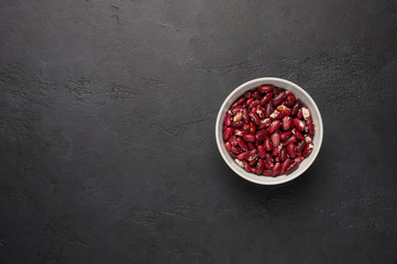 Bowl of red beans on a textured wooden black background. Vegetable protein healthy food