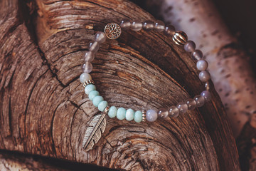 Mineral stone yoga bracelet with metal feather pendant on wooden background