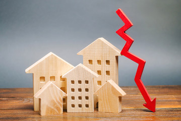 Miniature wooden houses and a red arrow down. The concept of low cost real estate. Lower mortgage...