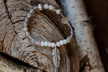 Mineral stone yoga bracelet with metal feather pendant on wooden background
