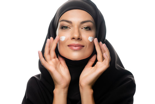 young Muslim woman in hijab applying cosmetic cream on chicks isolated on white