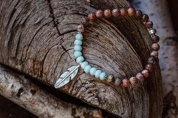 Mineral stone yoga bracelet with metal feather pendant on wooden background