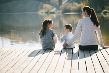 Mother and children relaxing next to a lake. They are smiling and talking on a sunny autumn day