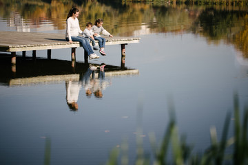 Fototapeta na wymiar Mother and children relaxing next to a lake. They are smiling and talking on a sunny autumn day