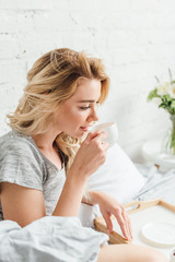 selective focus of beautiful blonde girl holding cup of coffee in bed