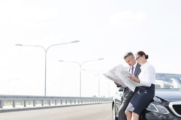 Business professionals analyzing map outside car on road against sky