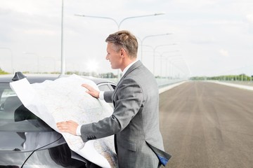 Businessman looking at the map outside broken car