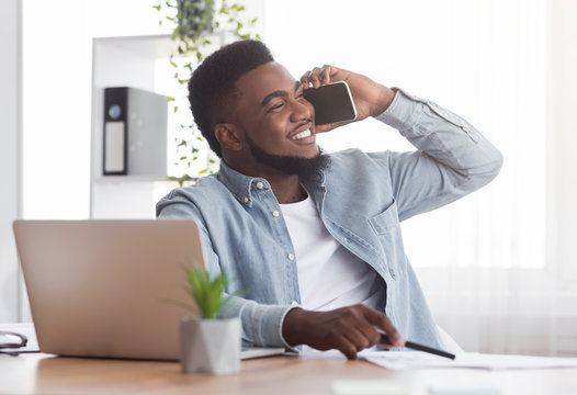 Smiling african american employee talking on mobile phone at workplace