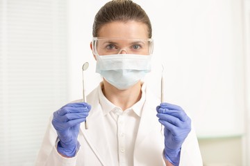 Confident dentist holding and showing dental cleaning tools in clinic