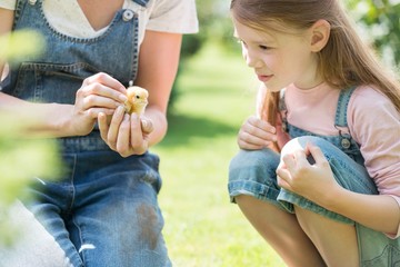 Farmer showing baby chick to her daughter in farm