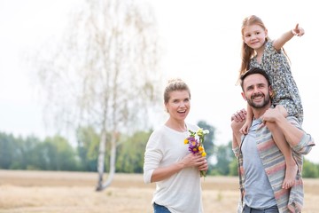 Father carrying his daughter on shoulders while walking with his wife in field