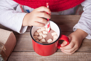 Child's hand holding red mug of Christmas cocoa on the wooden table