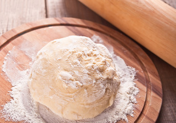 Raw dough for pizza or bread baking on wooden cutting board on black background