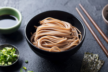 Soba noodles on a black bowl. Slate background. Close up.