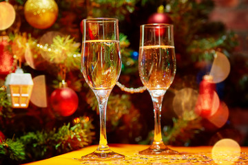 Two glasses of champagne on the background of a beautifully decorated balls, garlands, stars Christmas tree. Around the glow of rays and bokeh lights