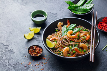 Stir fry noodles with vegetables and shrimps in black bowl. Slate background. Close up. Copy space.