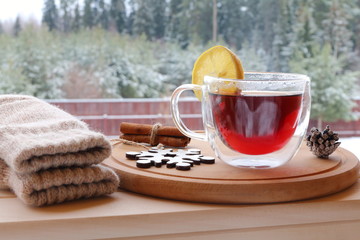 The glass mug of hot tea on the winter forest background. 