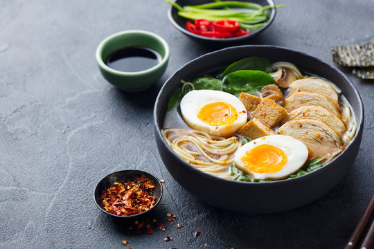 Asian noodle soup, ramen with chicken, tofu, vegetables and egg in black bowl. Slate background. Copy space.