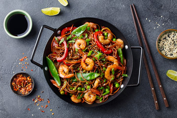 Stir fry noodles with vegetables and shrimps in black iron pan. Slate background. Top view.