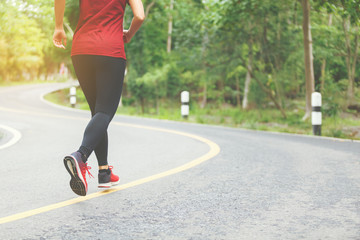 Legs of woman runner and runing at the road surround with green forest.