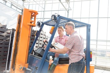 Senior farmer instructing young woman on how to drive forklift in Greenhouse