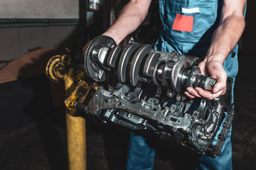 Auto mechanic installs a crankshaft in a disassembled engine.